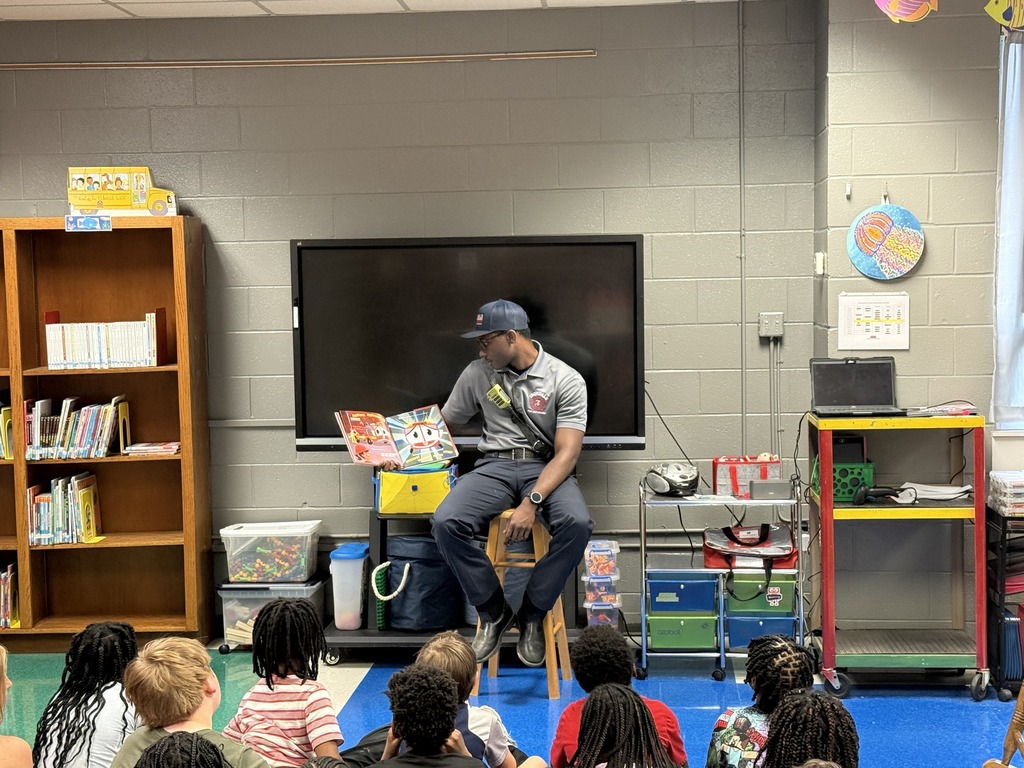 An Irondale Firefighter reads to a group of students. The firefighter sits on a stool and the students sit on the floor.