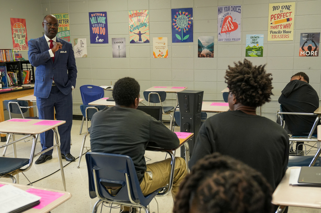 A man wearing a suit speaks to a classroom of students.