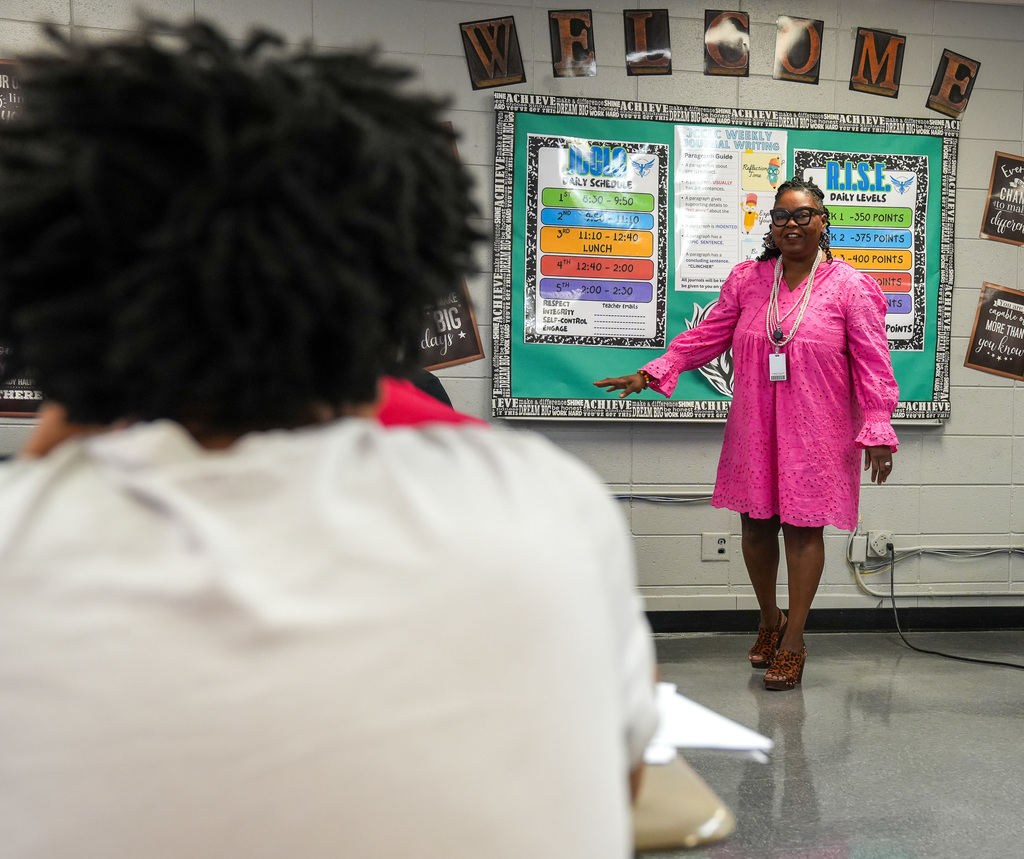 A woman wearing a bright pink dress smiles while she addresses a classroom of students.