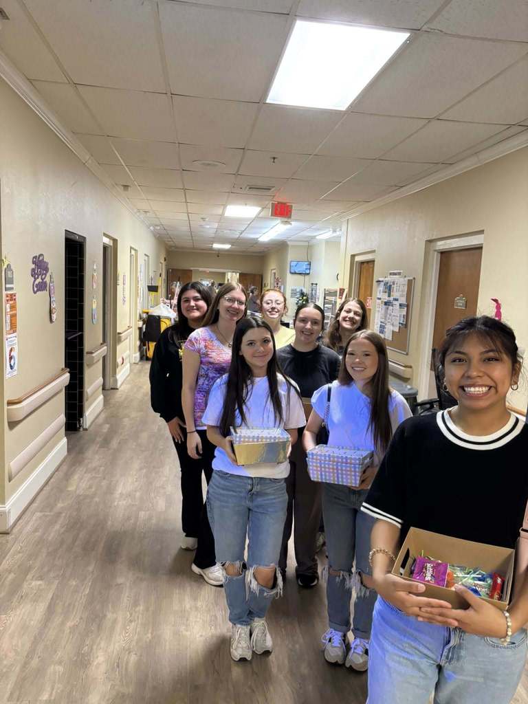 Corner High School students smile for a photo while standing inside a nursing home. They hold baskets of treats that they're giving out to the residents.