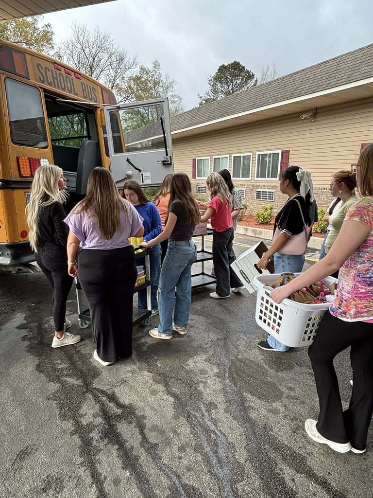Students unload care packages from a school bus while standing outside a nursing home.