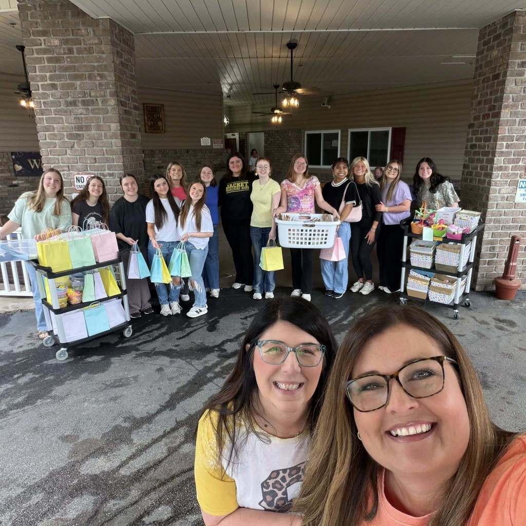 Corner High School students and employees stand for a photo and smile outside a nursing home. In front of the students are care packages they put together for the residents. 