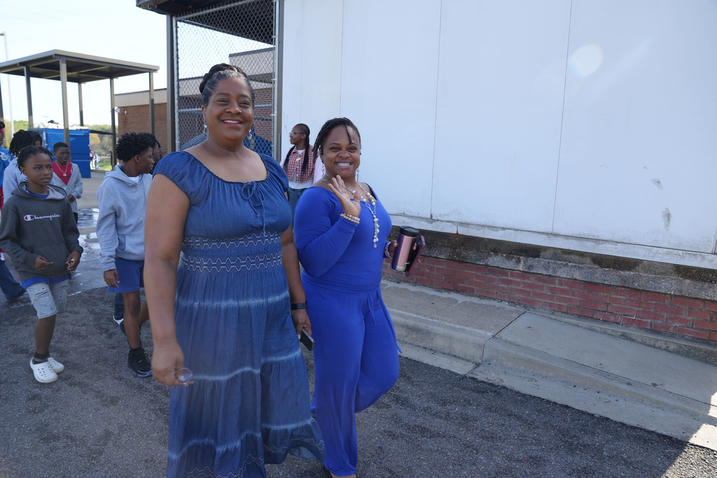 Two woman smile while walking outside of Erwin Middle School. Students walk behind them.