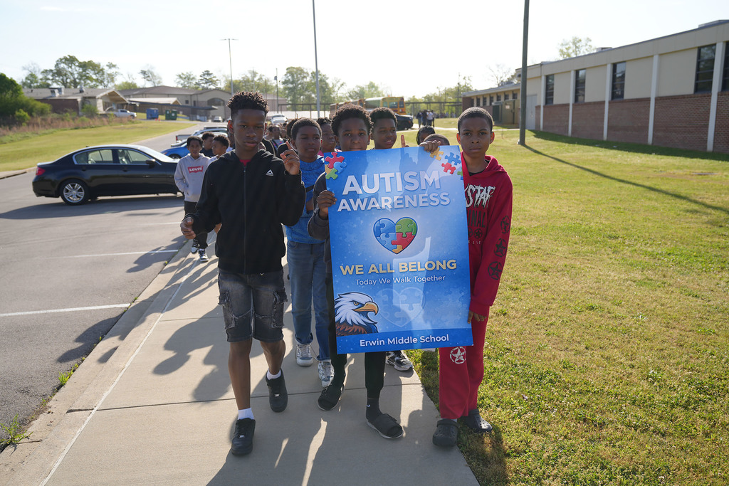 Erwin Middle School students walk outside the school and hold a sign that says "Autism Awareness We All Belong Today We Walk Together Erwin Middle School."