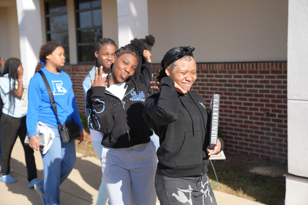 Students walk outside of Erwin Middle School. Two students in the front of the picture smile. One of the students holds up a peace sign.