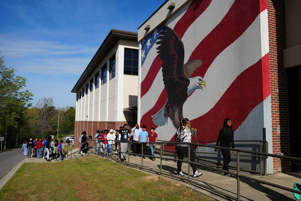 Students walk outside of Erwin Middle School. They walk on the sidewalk outside a large mural of an Eagle and an American flag.