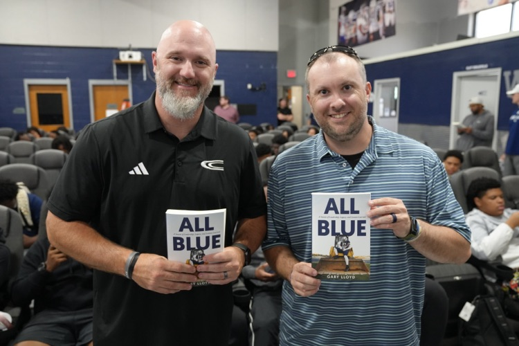 CCHS football coach Stuart Floyd poses next to Gary Lloyd for a photo in the school’s field house. They both hold copies of the book “All Blue: A Season of Leadership, Legacy, and Lessons Learned."