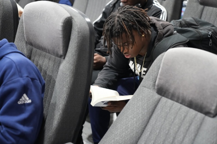 A CCHS football player reads a copy of All Blue: A Season of Leadership, Legacy, and Lessons Learned while sitting in the field house  