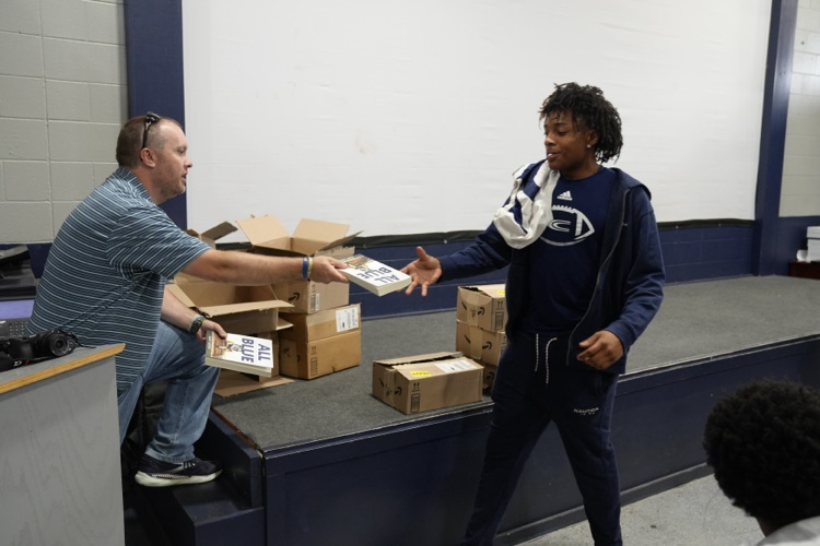 A man hands a Clay-Chalkville High School football player a book inside the school’s field house  