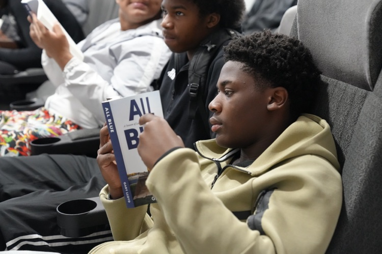 A CCHS football player reads a copy of All Blue: A Season of Leadership, Legacy, and Lessons Learned while sitting in the school’s field house  