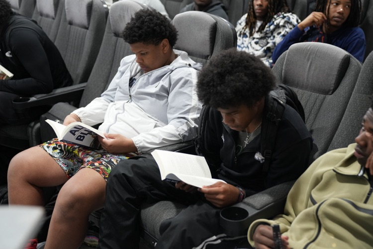 Students sit in the CCHS field house and reads copies of “All Blue: A Season of Leadership, Legacy, and Lessons Learned"