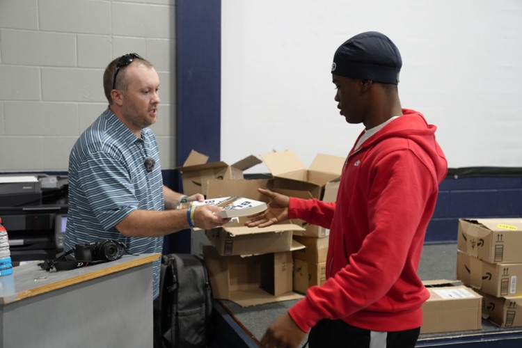 Gary Lloyd hands a CCHS football player a book while they stand in the school’s field house  
