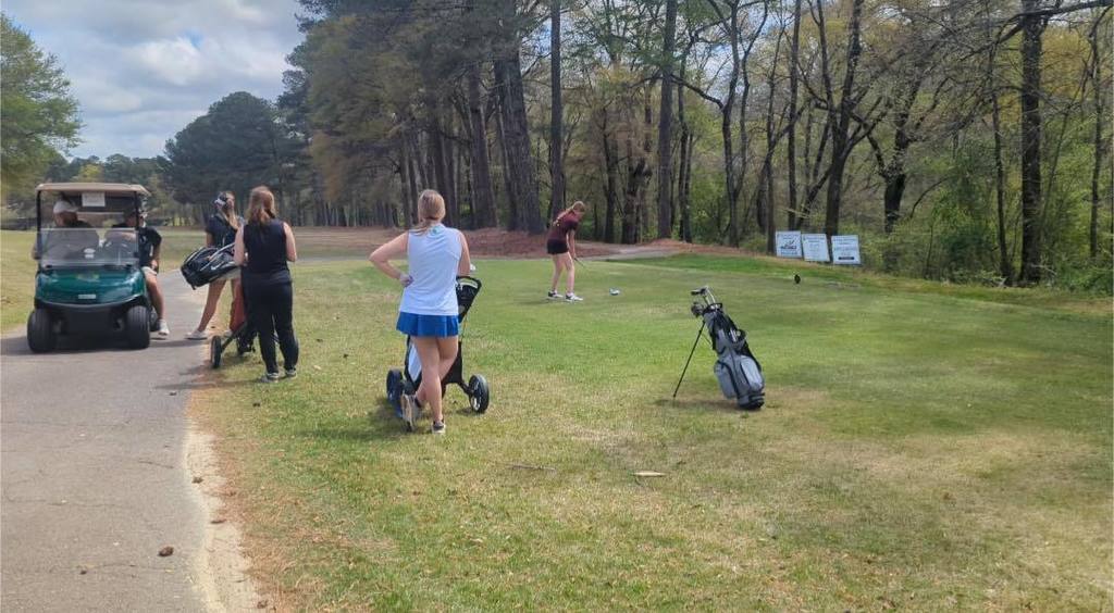Kennedy McAnnally gets ready to put while competing at an outdoor golf course. Other golfers stand around her.