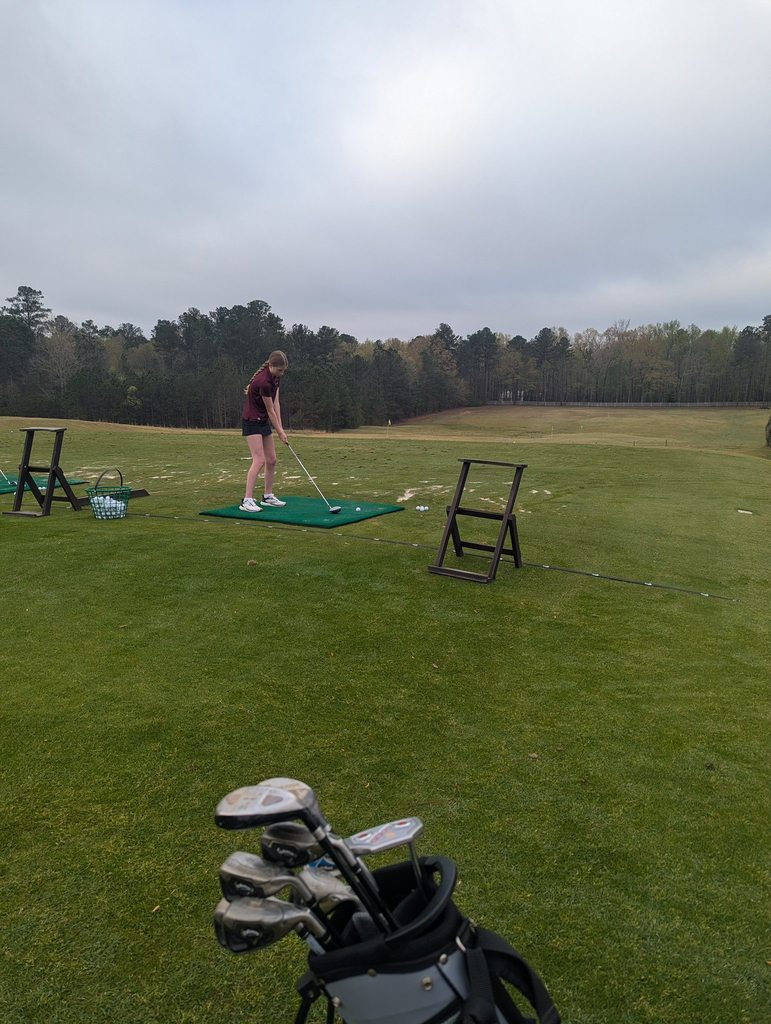 Kennedy McAnnally holds a golf club while standing at an outdoor golf course. She gets ready to hit the golf ball.