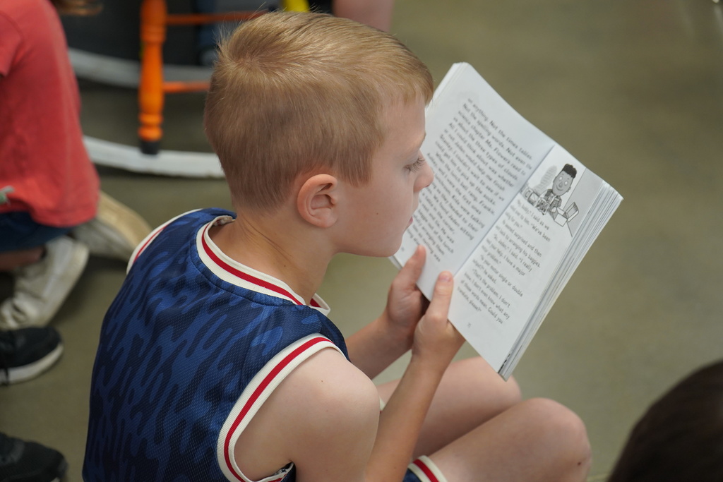 A student sits in a classroom and reads a chapter book.