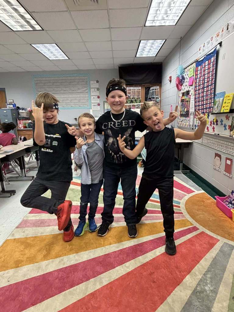 A group of students stand together and pose for a photo. They make rock and roll symbols with their hands and dress in rock and roll themed outfits.