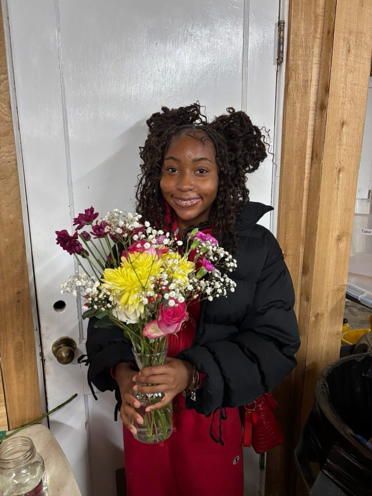 A student smiles while holding a bouquet of flowers and standing in a room.