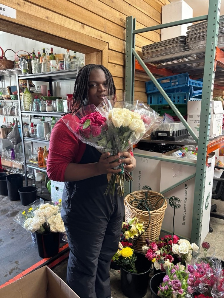 A student smiles while holding a bouquet of flowers and standing inside a room  