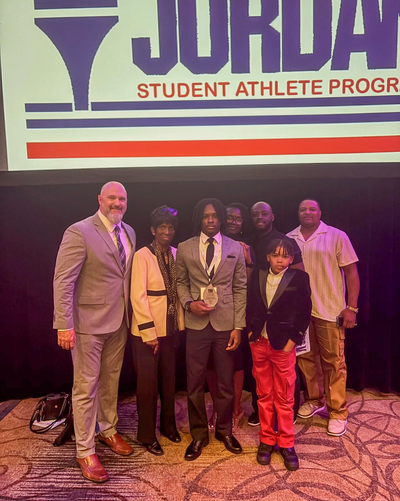 Clay-Chalkville High School football coach Stuart Floyd and football player Brayden Butler pose with Brayden's family for a photo in a ballroom. Brayden holds a Bryant-Jordan Student-Athlete Achievement Award in his hand.