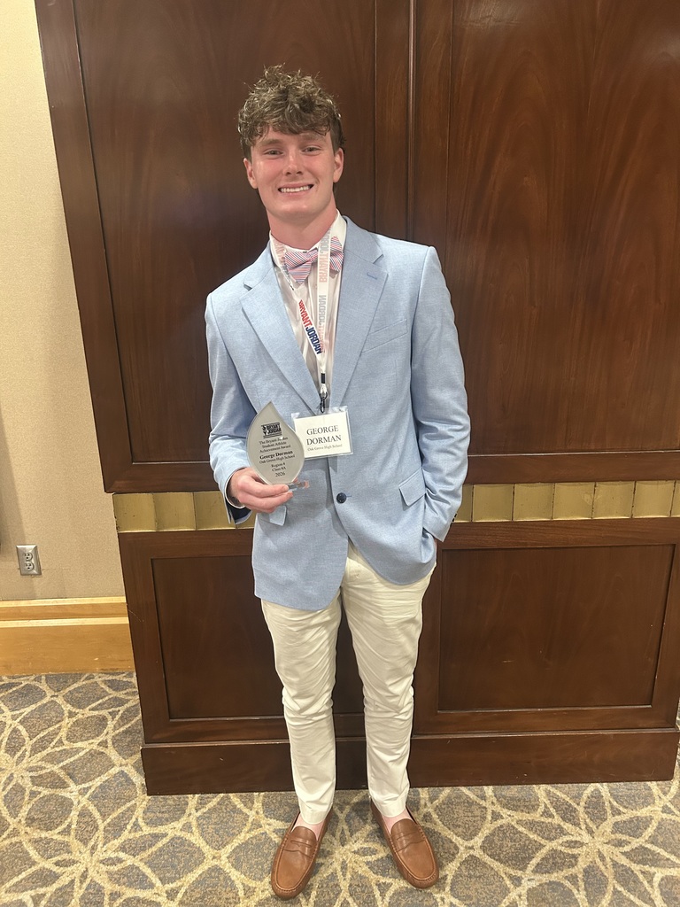 Oak Grove High School student George Dorman smiles for a photo. He wears a suit and stands inside a room. He holds his Bryant-Jordan Student-Athlete Achievement Award in his hand.