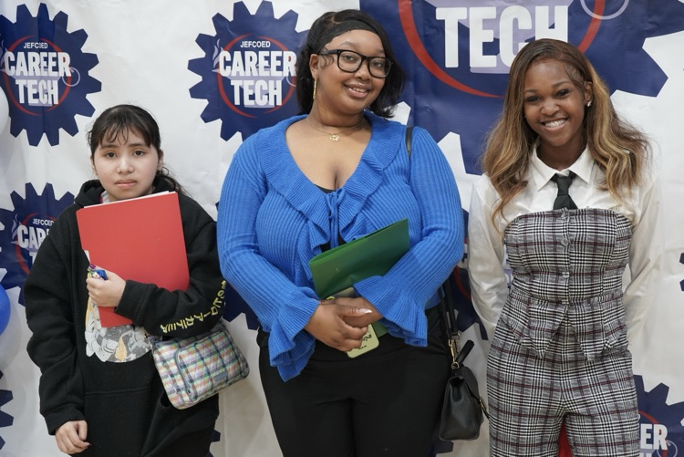 A group of girls stand together for a photo and smile in front of a backdrop that says Jefcoed Career Tech.