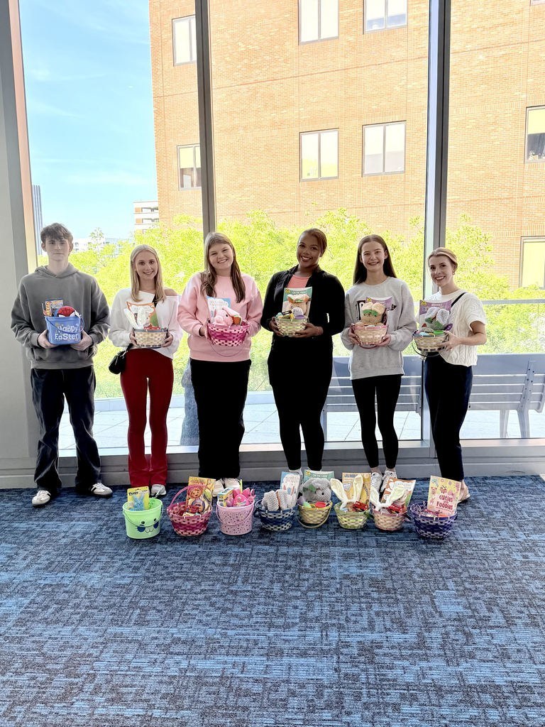 A group girls and one boy stand together for a photo inside Children's of Alabama and smile. They hold baskets with toys and activities inside them.