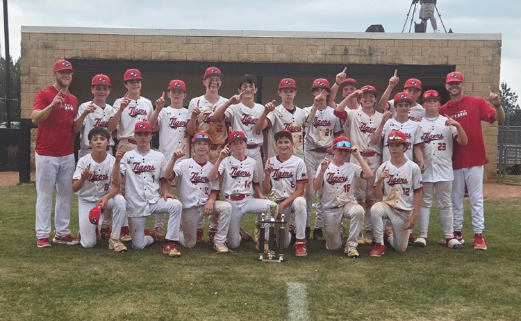 Oak Grove Middle School’s baseball team and coaches stand together for a photo on the baseball field and hold up number 1s with their hands.