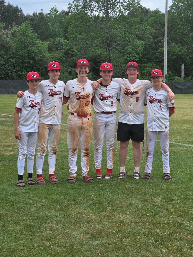 Oak Grove baseball players stand together for a photo and smile while standing on a baseball field  