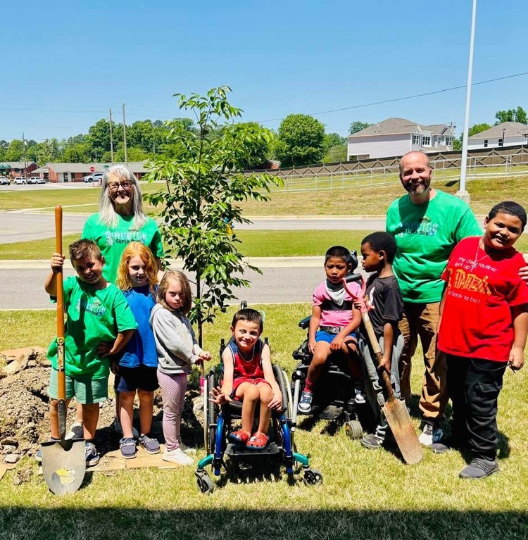 A group of students smile together for a photo outside of school after planting a tree.