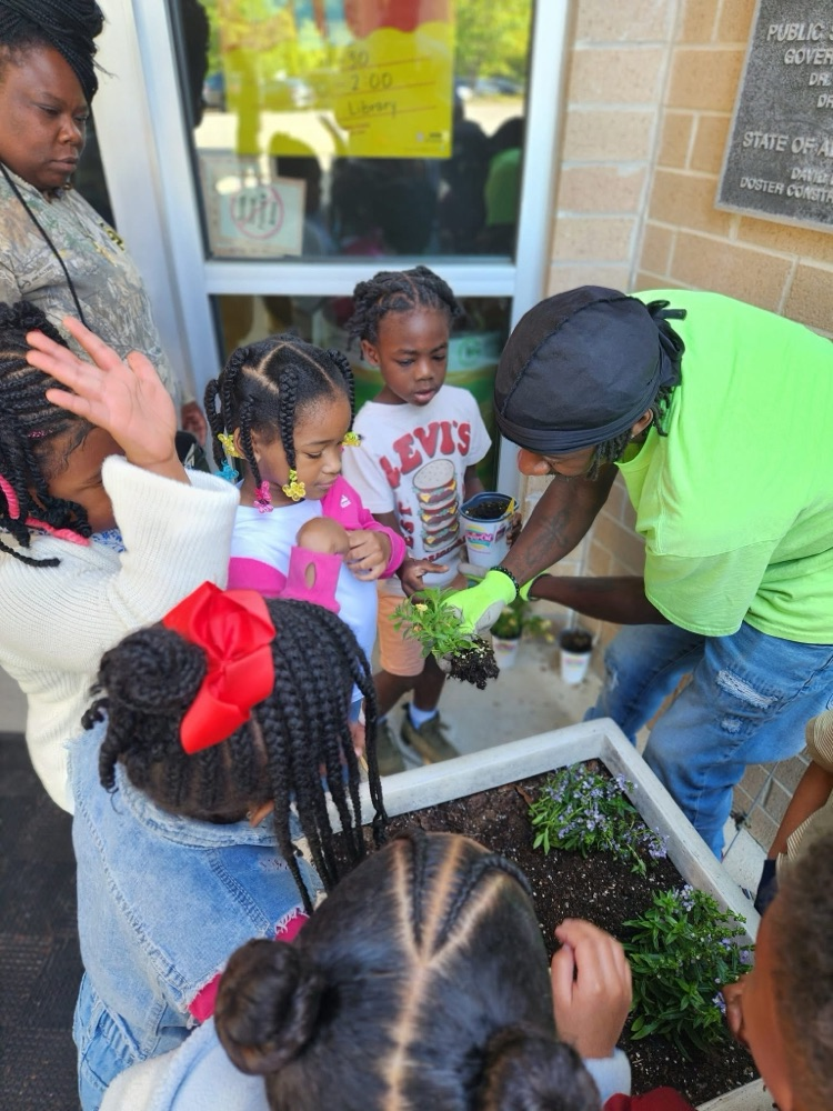 A man shows a group of students a plant while they stand over a garden bed.