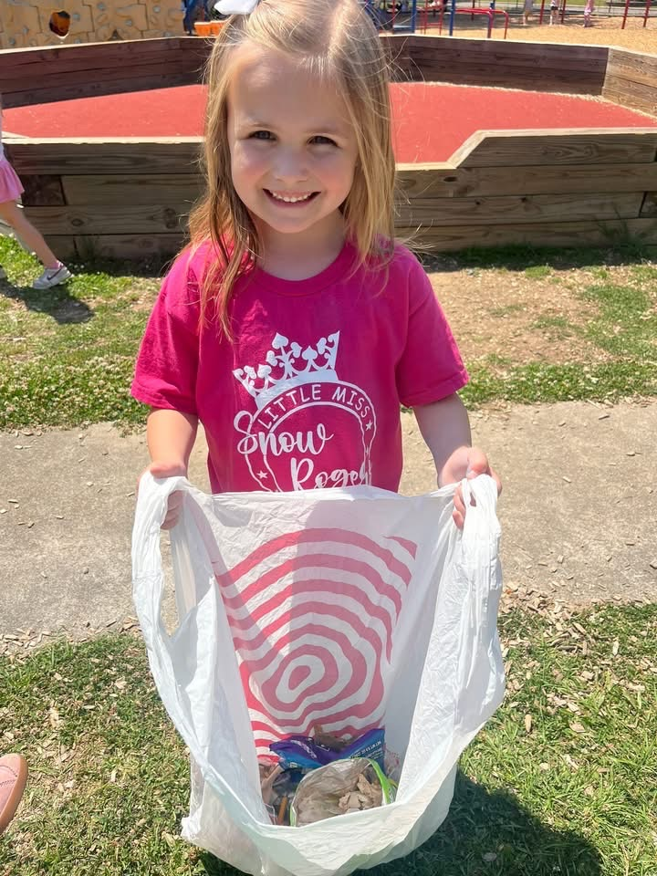 A girl holds a plastic bag filled with trash and smiles for a photo.