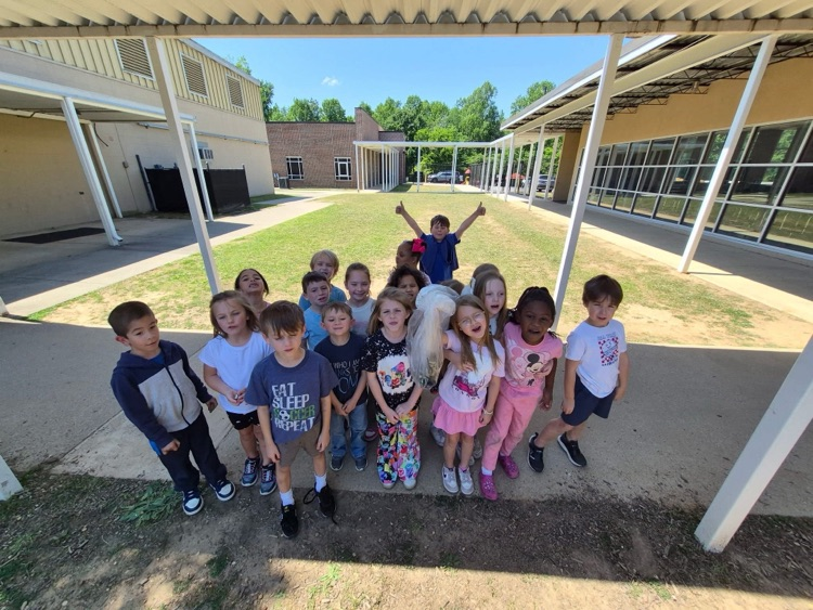 A group of students stand outside a school and smile for a photo while holding a bag of trash they collected from outside.