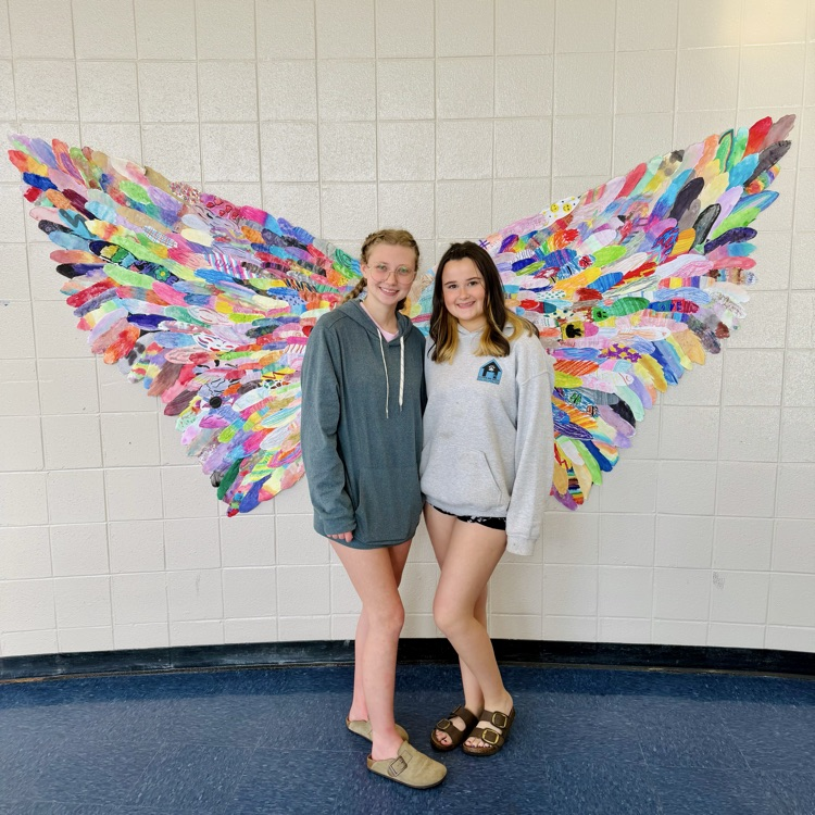 2 girls in front of art piece of butterfly wings