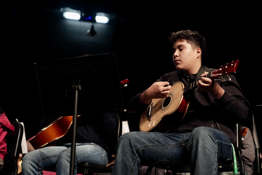 A boy plays guitar while sitting on a stage.