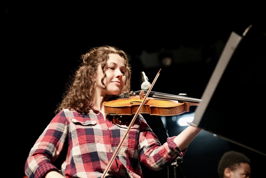 A girl plays the violin while sitting on a stage.