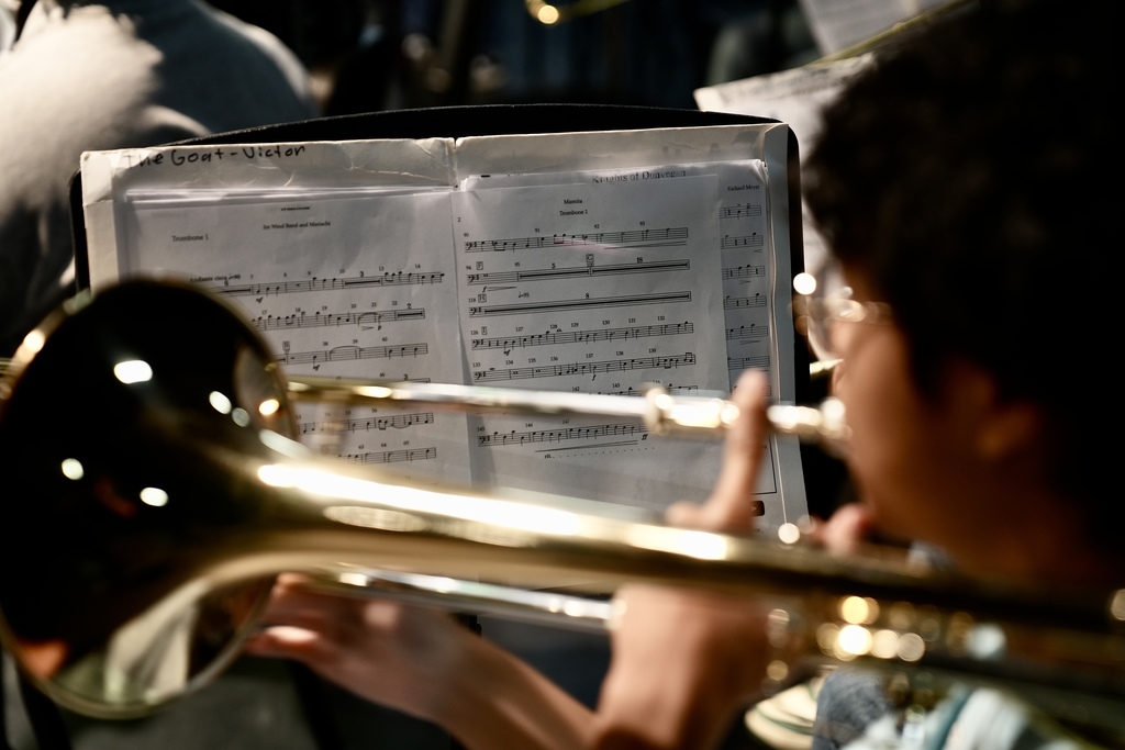 A student plays a trumpet on a stage while sitting in front of sheet music.