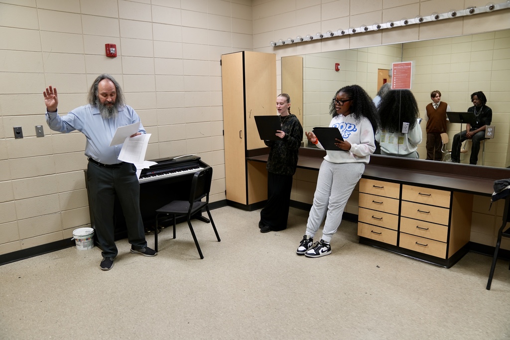 A man and two girls rehearse a song while standing in a dressing room.