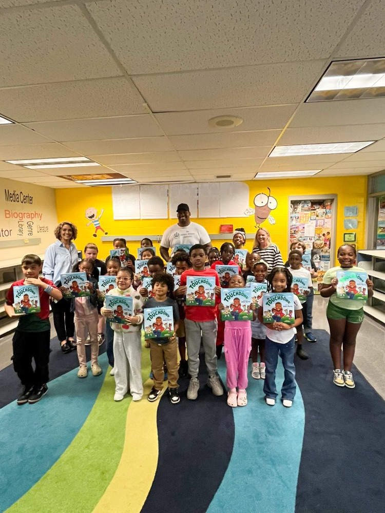 Quinnen Williams stands with a classroom of students and their teacher. They all smile and hold up picture books.