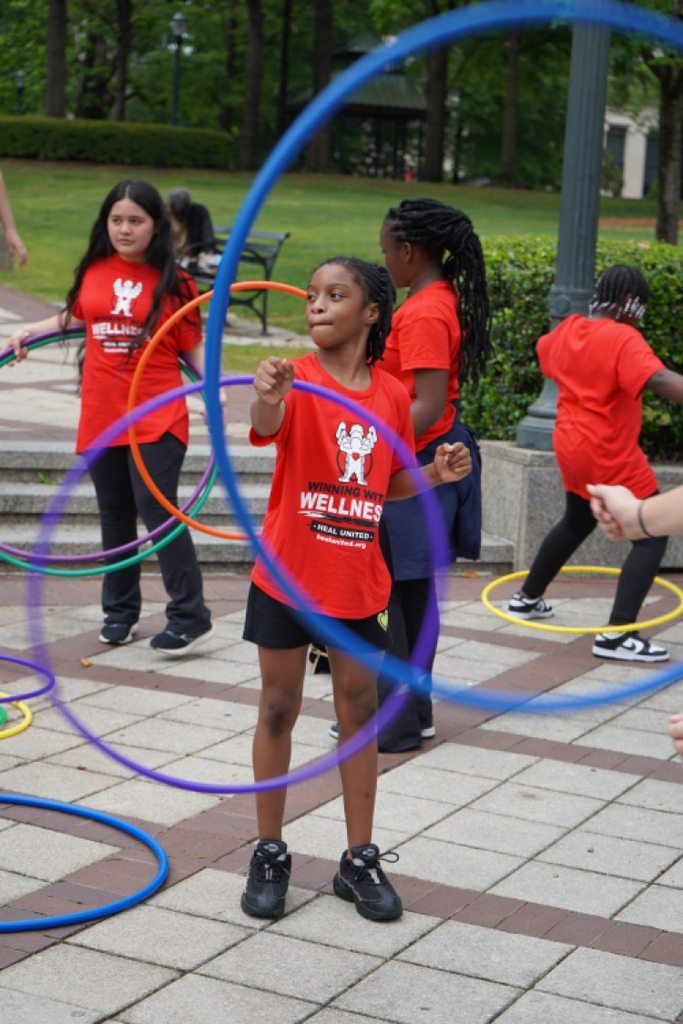 Students play with hula hoops at a park. They wear matching “Healthy Eating Active Living” shirts.