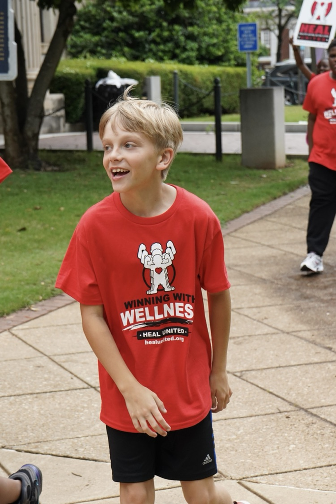 A student wearing a “Healthy Eating Active Living” shirt smiles while walking down a sidewalk.