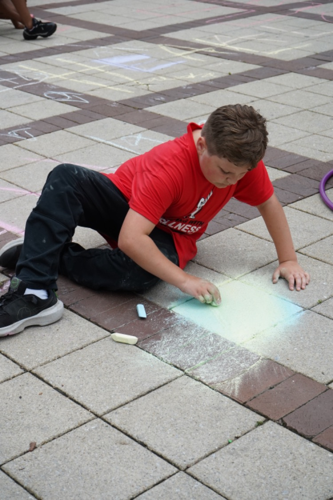 A student draws on a sidewalk with chalk.