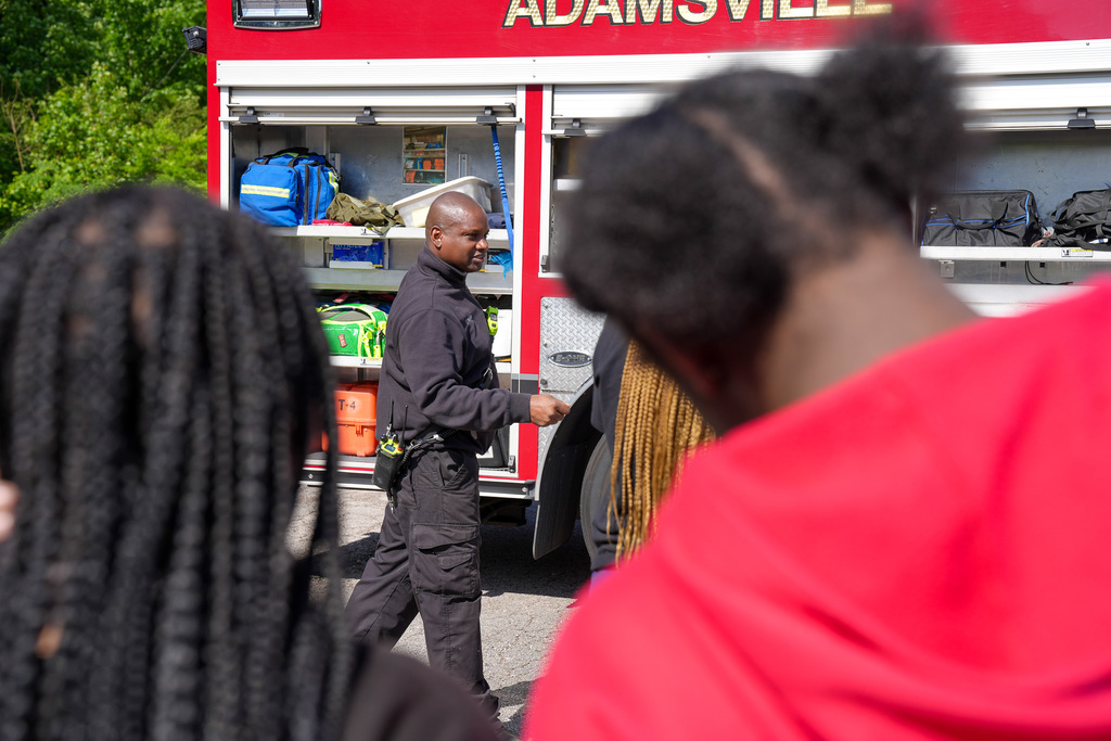 A firefighter stands outside a fire truck and speaks to students.