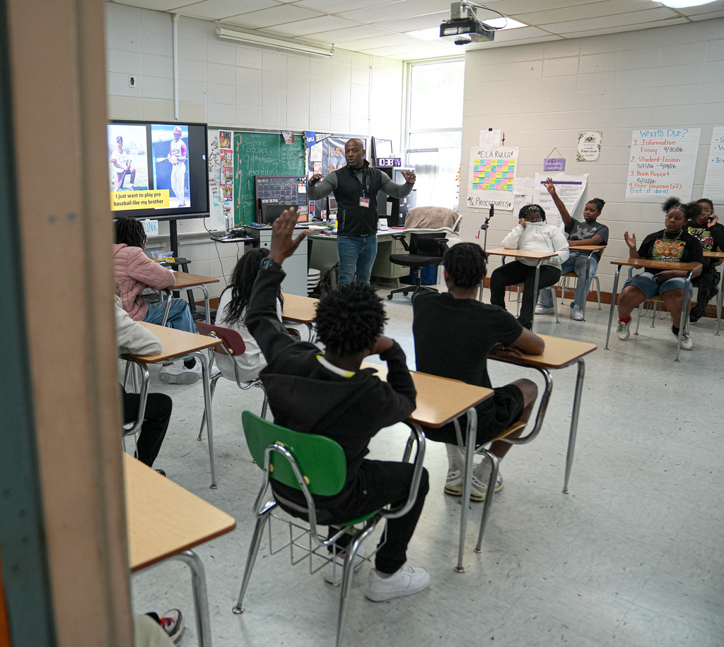 A man speaks to a classroom of students. Some of the students raise their hands.