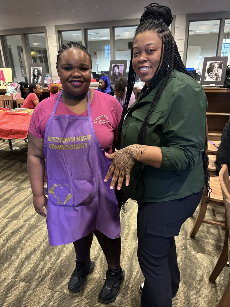 A student and a teacher stand together for a photo in the Hueytown High School library. The teacher shows off her henna tattoo done by the student.
