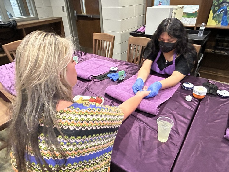 A student gives a teacher a hand massage inside a school library.