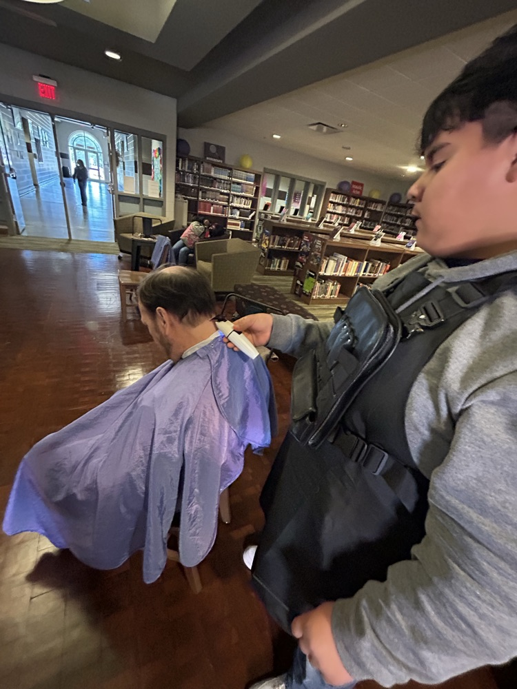 A student gives a teacher a haircut inside the school library.