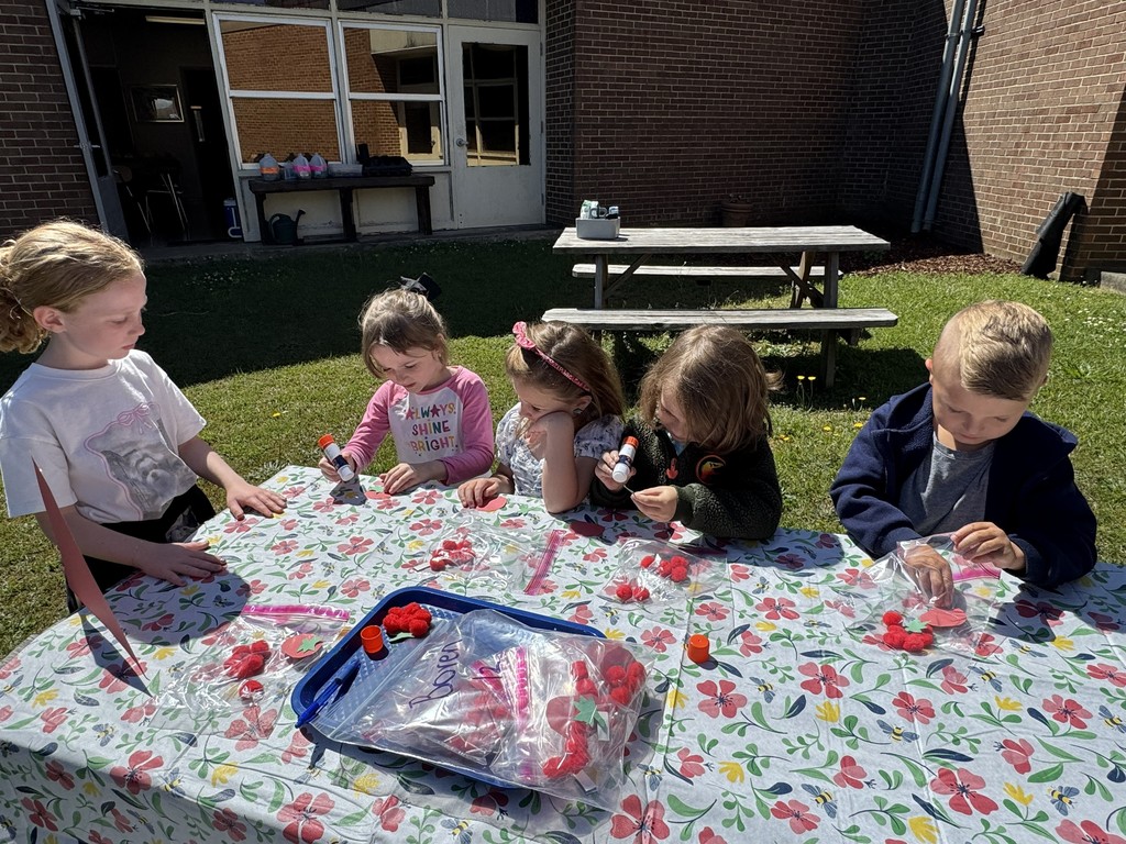 A fourth grade student looks on while Pre-K students work on a garden craft with pom-poms and glue sticks.