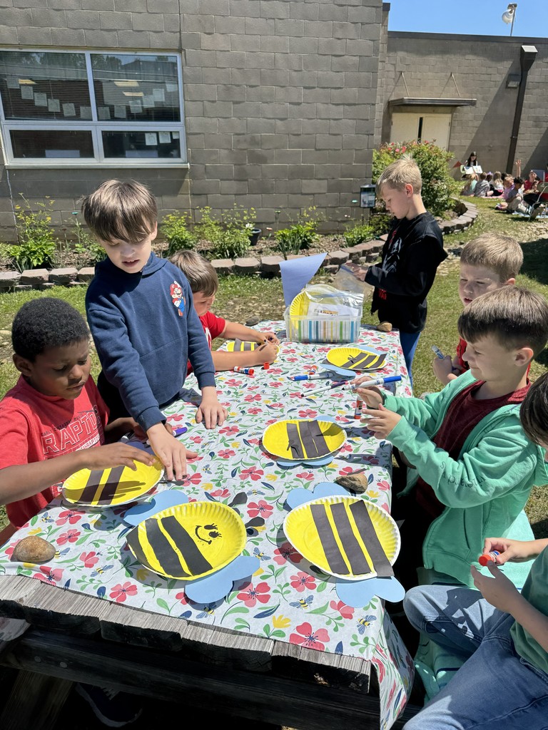 4th grade students assist younger students to work on a bee craft using construction paper and paper plates.