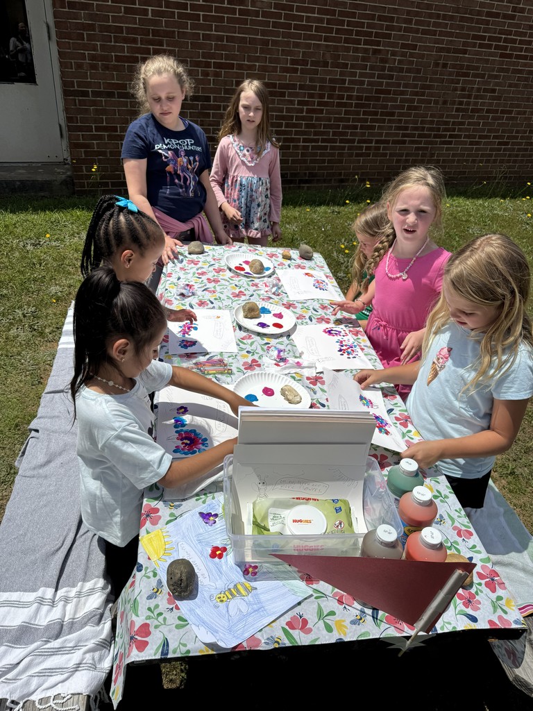 Fourth grade girls assist kindergarten students to complete a garden craft using paint and paper plates.