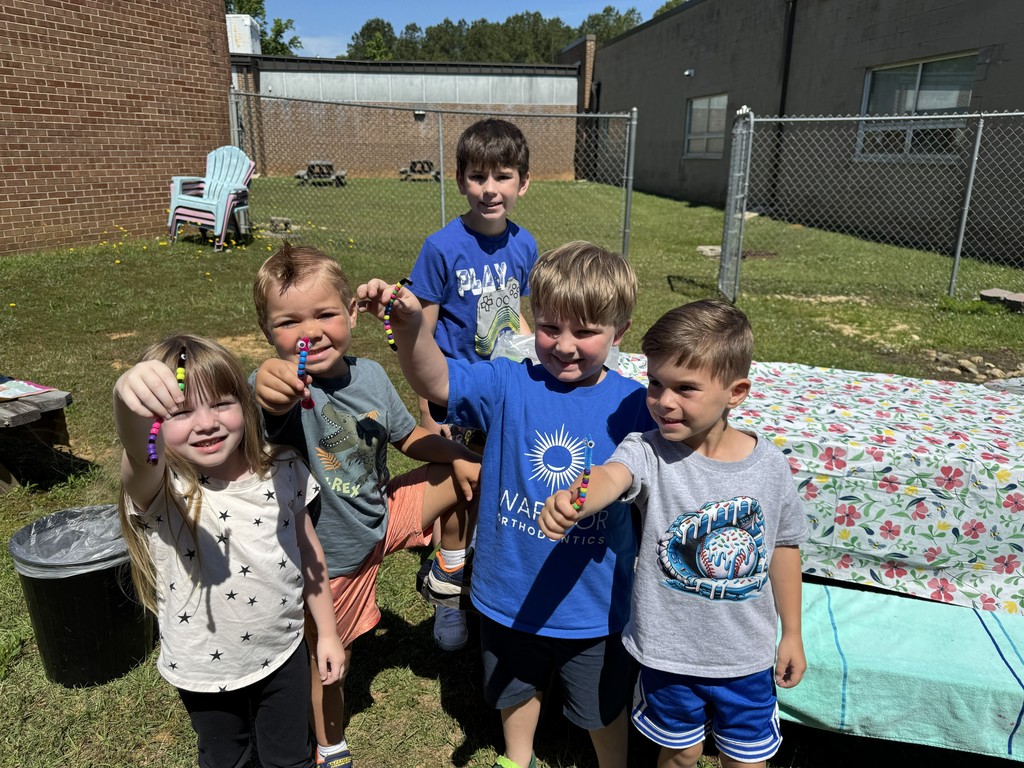 Pre-K students hold up the inchworm craft they completed in the Bryan garden. A fourth grade student looks on.